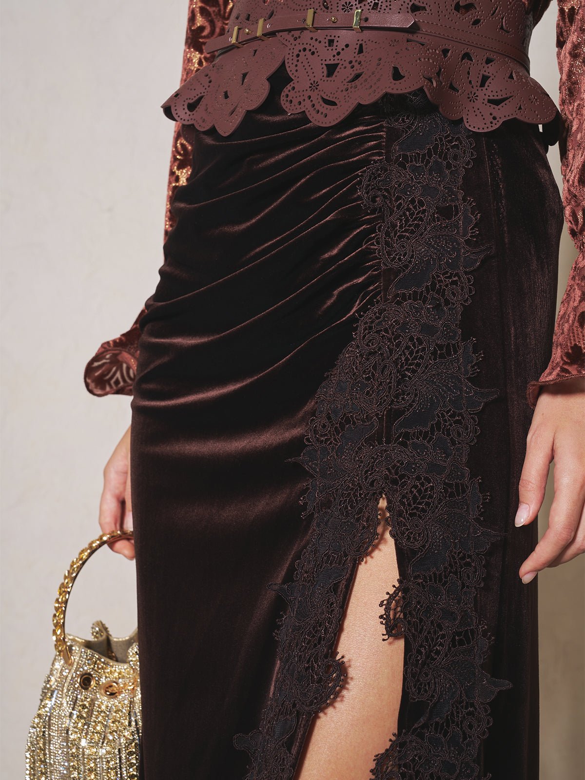 A person holds a gold beaded handbag while wearing Social Queen's Pleated Lace-Panel Velvet Skirt; only their lower torso and hand are visible.