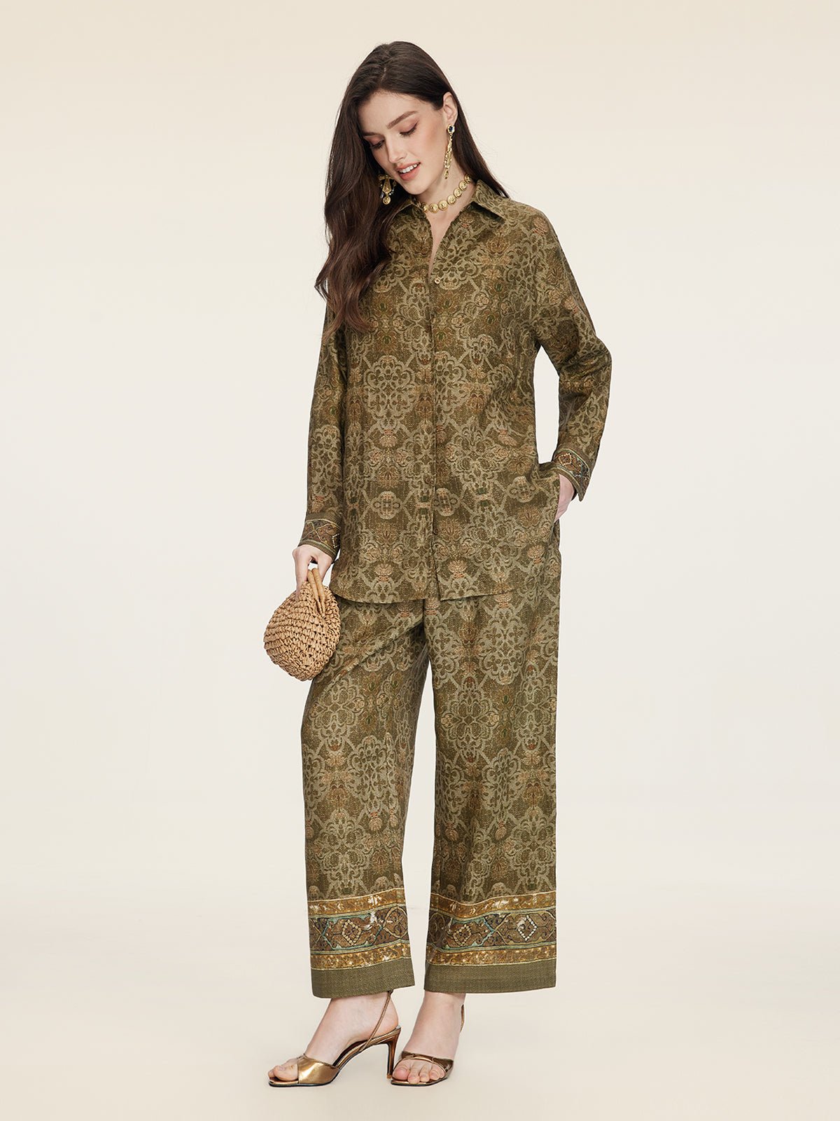 A woman wearing the Social Queen Printed Linen Blouse, paired with gold sandals and a woven handbag, accessorized with jewelry, stands against a plain background.