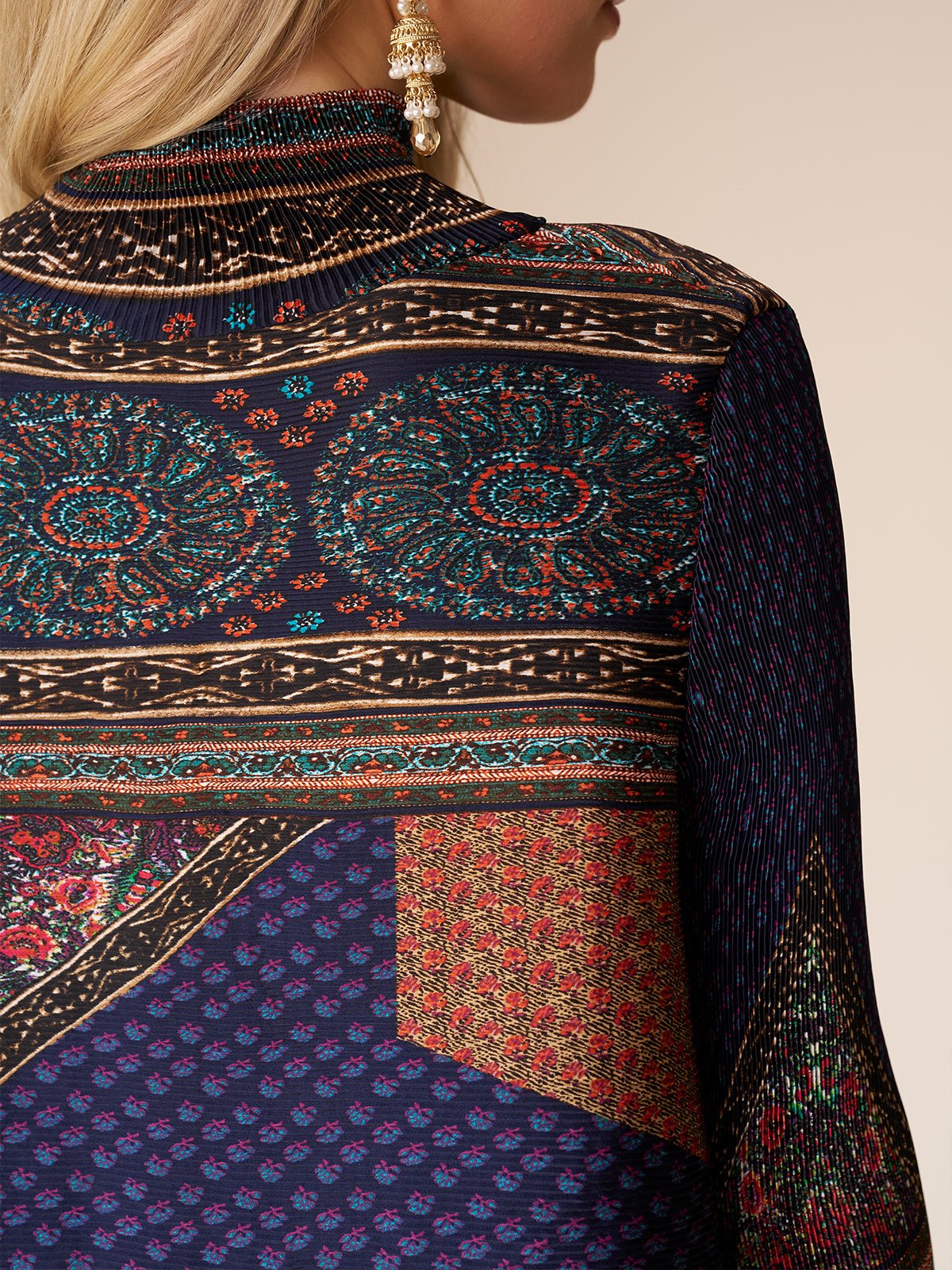 A close-up of a woman's back wearing the Social Queen Retro Ethnic Print Pleated Dress, featuring vibrant patterns and pleats, paired with a gold earring.