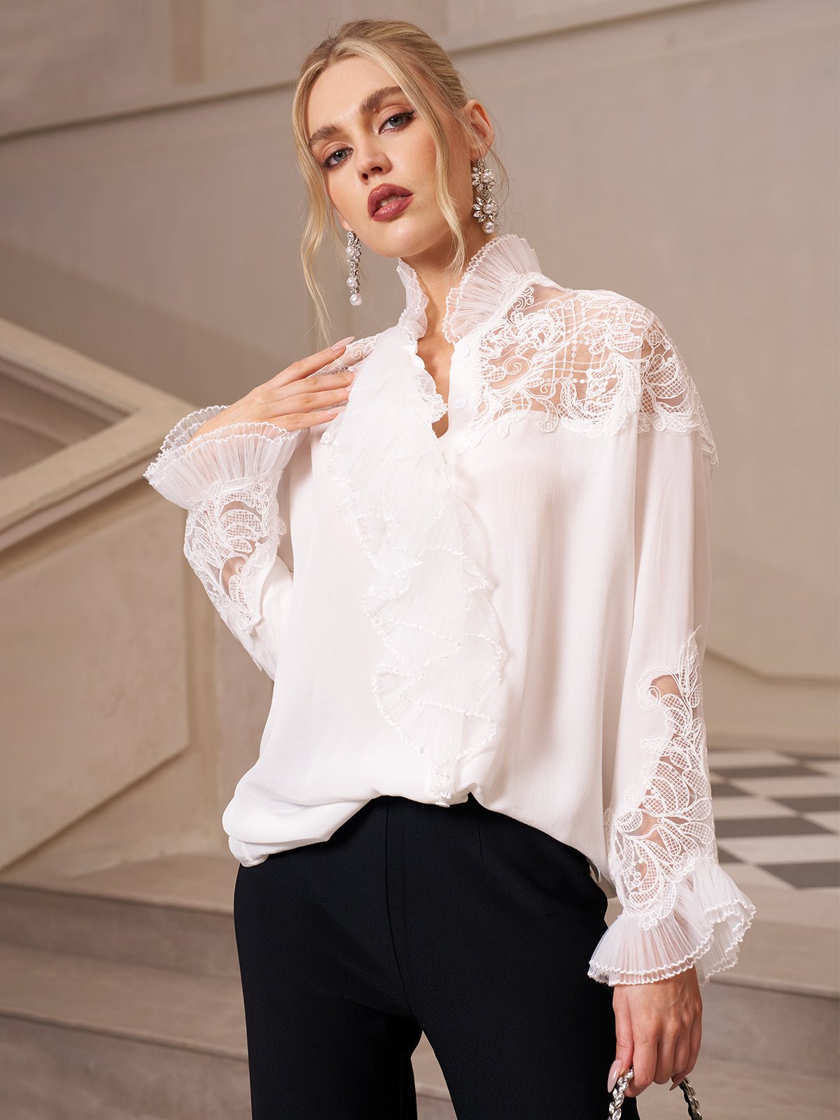 A woman wearing a Social Queen Ruffled Lace Blouse with Asymmetric Hem and black pants stands indoors by a staircase, looking at the camera.