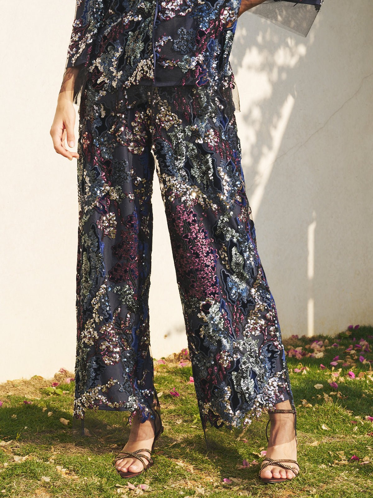 A person stands outdoors in Social Queen’s Sequin Embroidered Mesh Wide-Leg Pants and heeled sandals. Only the lower body is shown, sunlight casting shadows—an ideal choice for a stylish wedding guest look.