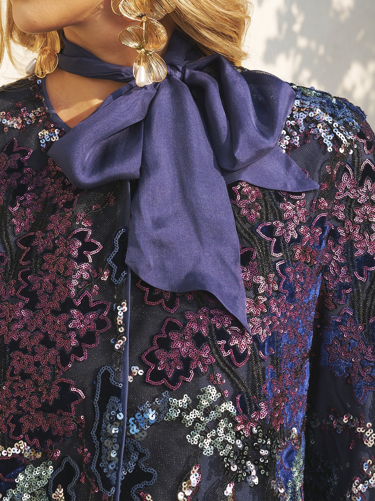 Close-up of a person wearing Social Queen’s Sequin Embroidered Velvet Mesh Jacket with a large matching bow at the neck and gold earrings—ideal for a chic party celebration.
