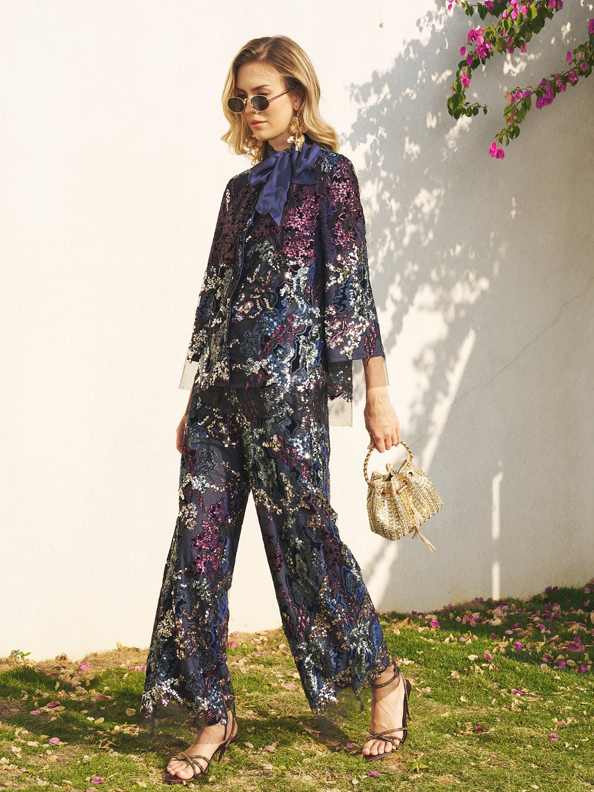 A woman in sunglasses stands outdoors wearing a dark floral set and the Social Queen Sequin Embroidered Velvet Mesh Jacket, styled with a navy neck bow and a small woven handbag.