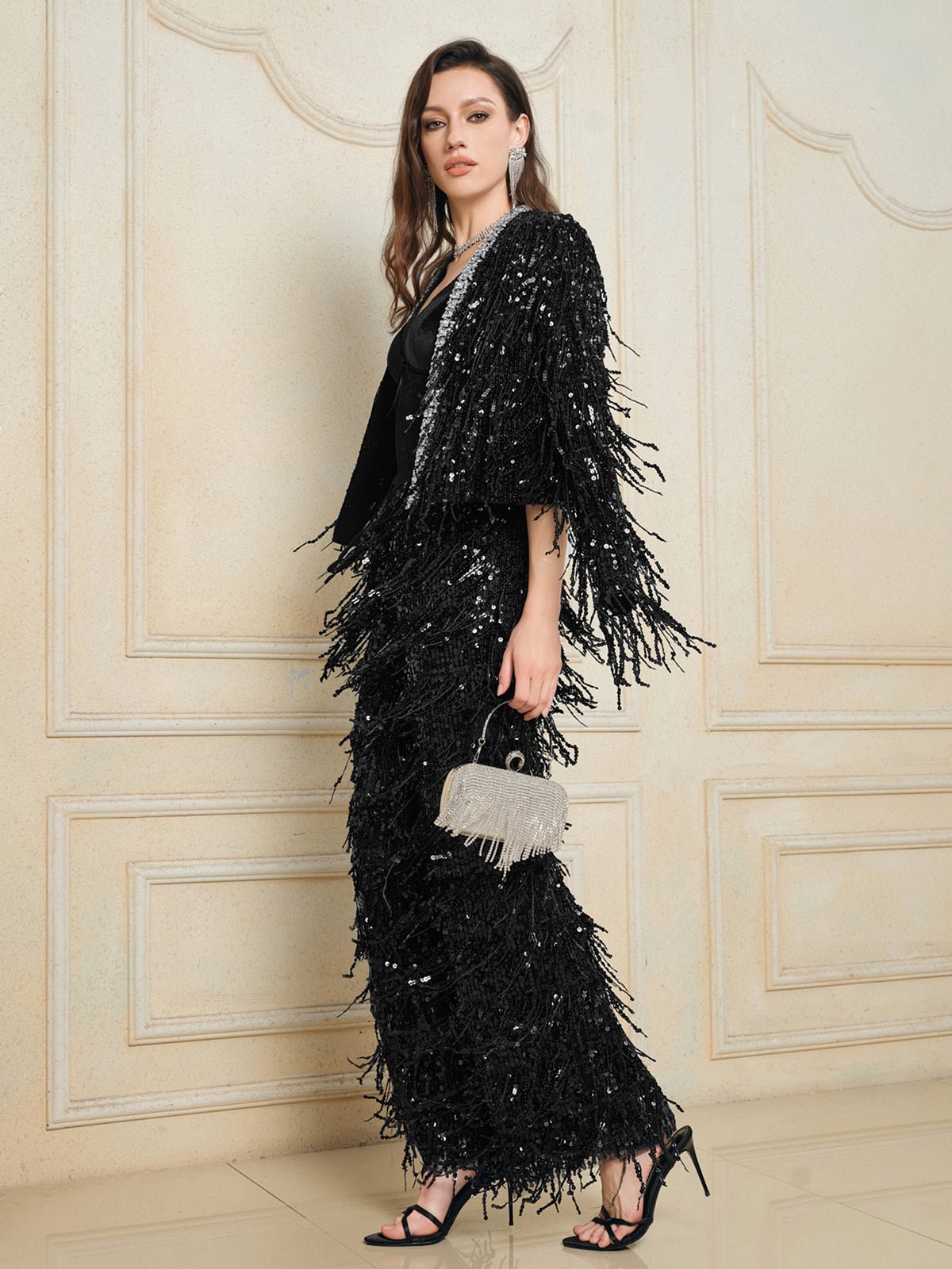 A woman wears Social Queen's Sequin Fringe Wide-Leg Pants, holding a silver fringed handbag in front of a cream-paneled wall.