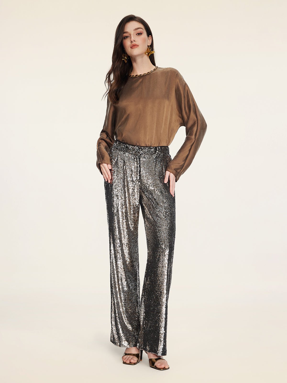 A woman wears Social Queen's Sequin High-Waist Wide-Leg Pants with a brown long-sleeve blouse, black sandals, and statement earrings against a plain background.