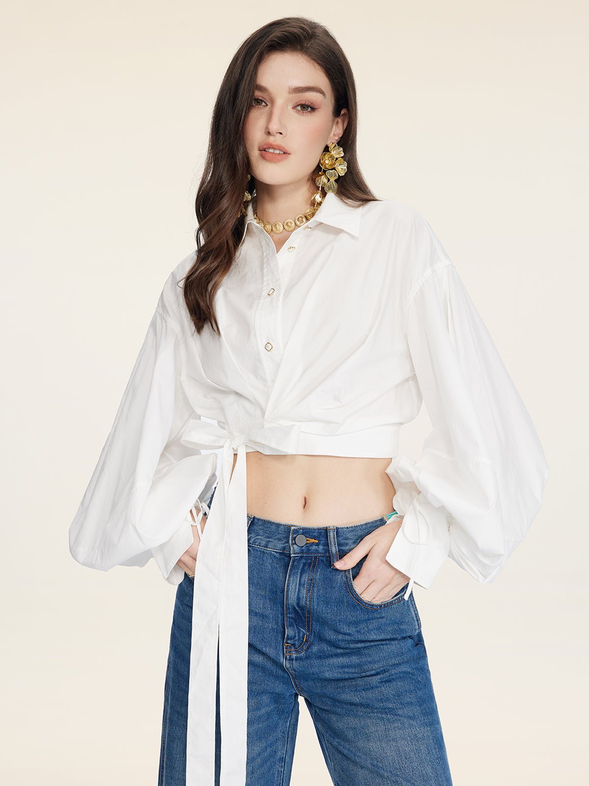 A woman poses in the Social Queen Tie-Neck Silk Lantern Sleeve Blouse, styled with blue jeans, large gold earrings, and a necklace.