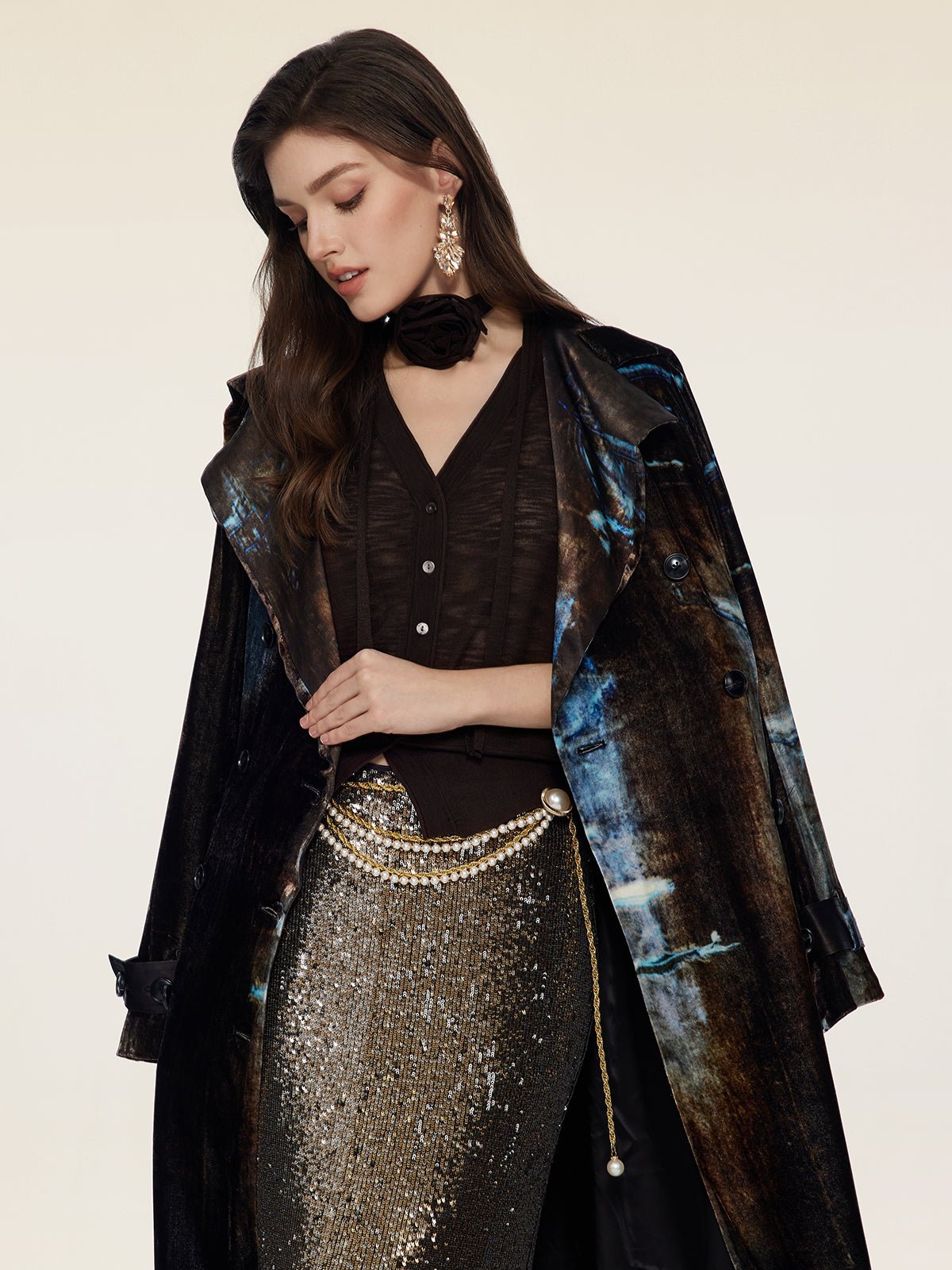 A woman wears the Social Queen Velvet Gradient Tie-Waist Trench Coat, paired with a black top, metallic sequin skirt, pearl belt, and statement earrings, standing against a plain light background.