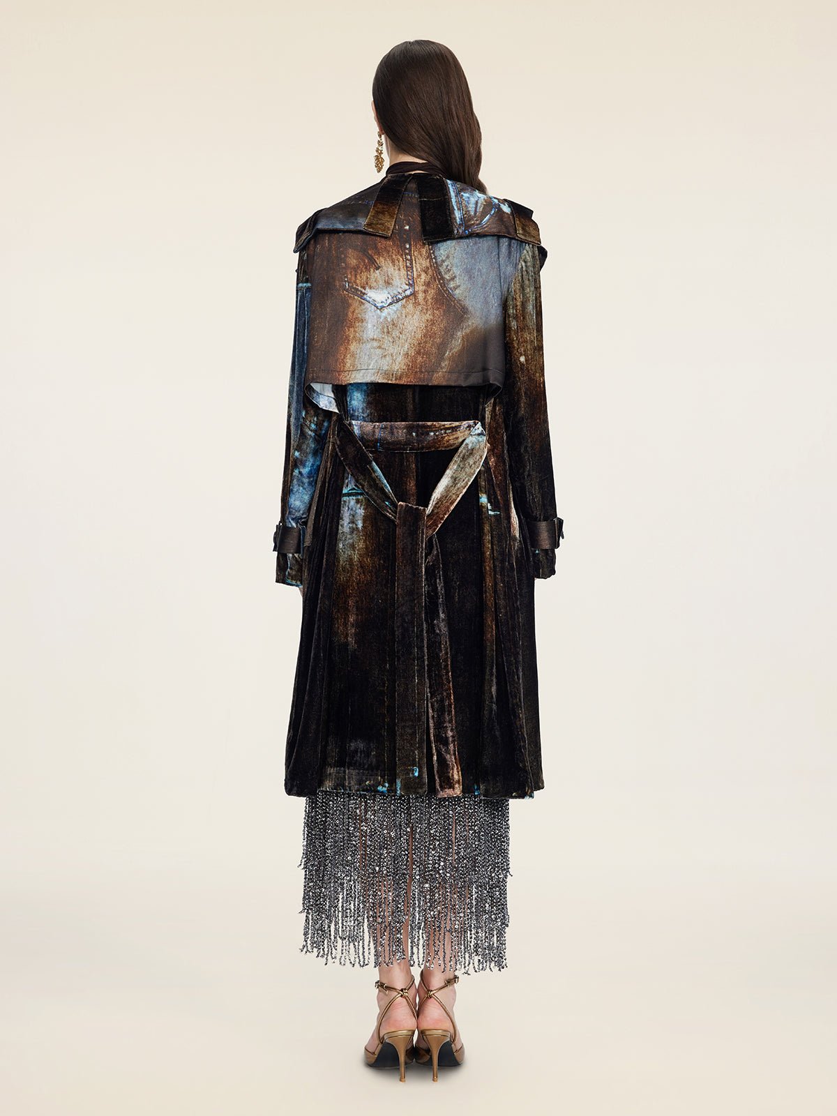 A woman faces away in a Social Queen Velvet Gradient Tie-Waist Trench Coat, styled over a silver beaded fringe skirt and strappy heels, set against a plain background.