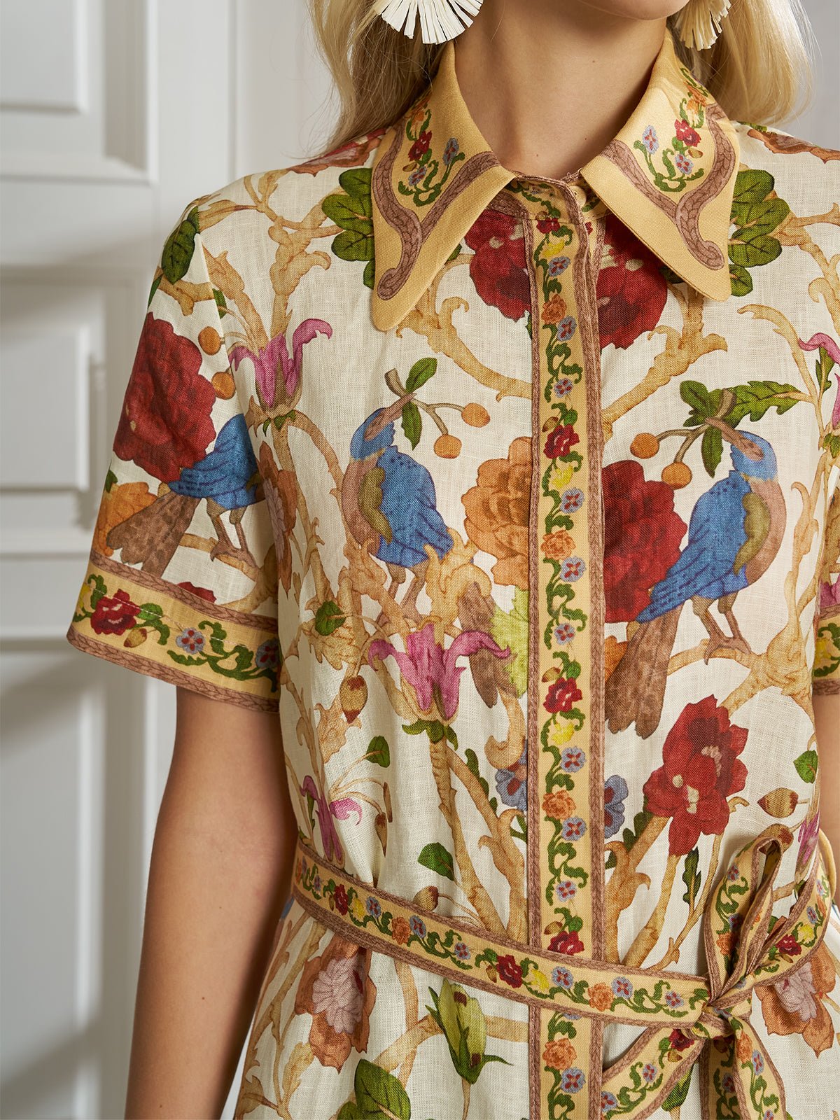 A woman wears the Social Queen Vintage Floral & Bird Print Shirt Dress with short sleeves, standing before a white paneled door—a perfect choice for sunny resort days.