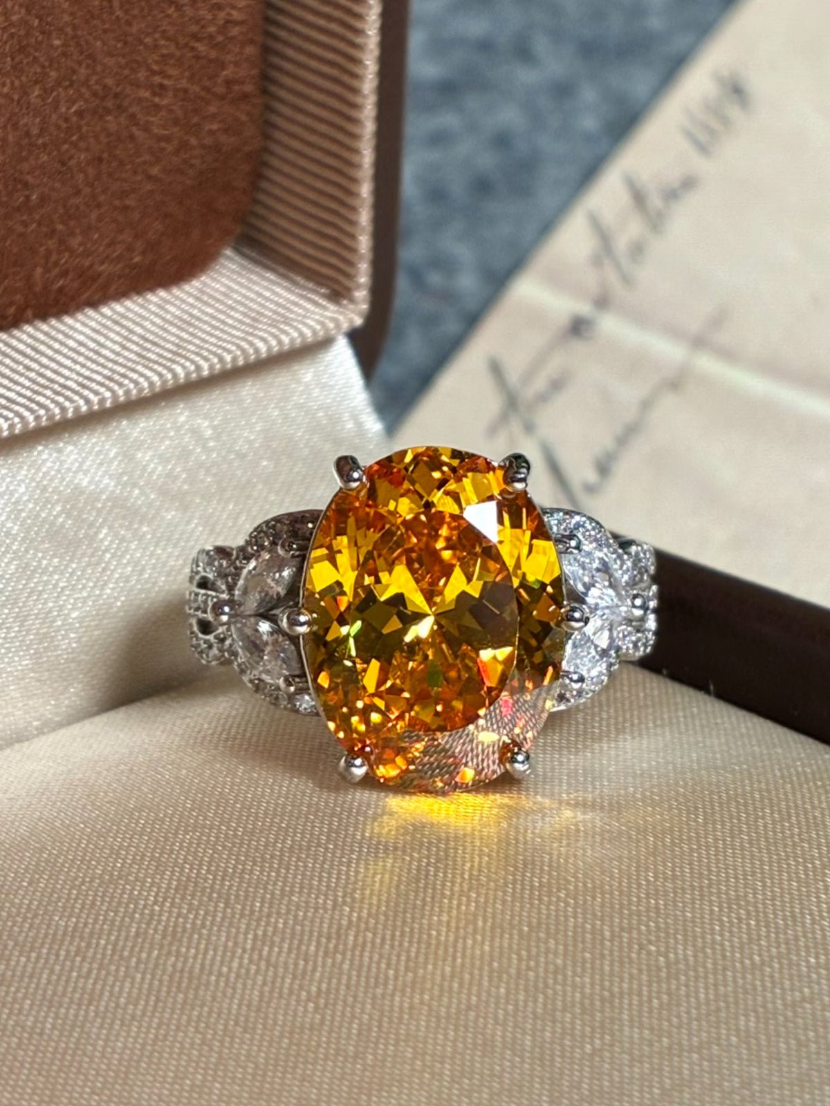 Make a statement with the Social Queen Yellow Crystal Ring, an adjustable white gold piece featuring a large yellow crystal center and smaller clear accents, elegantly presented in a beige ring box.