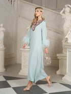 A woman in the Social Queen 100% Mulberry Silk Feather Limited Dress—a light blue vintage-inspired gown with ostrich feather sleeves and embellished neckline—holds a beaded handbag while walking indoors by classical statues.