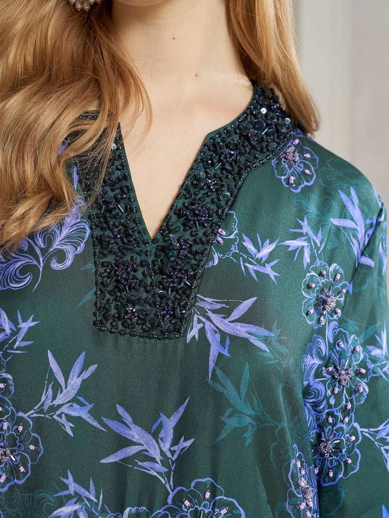 Close-up of a person wearing the Social Queen 100% Mulberry Silk Printed Beaded Dress, featuring a dark green hue, V-neckline with beading, and a purple floral bamboo print.