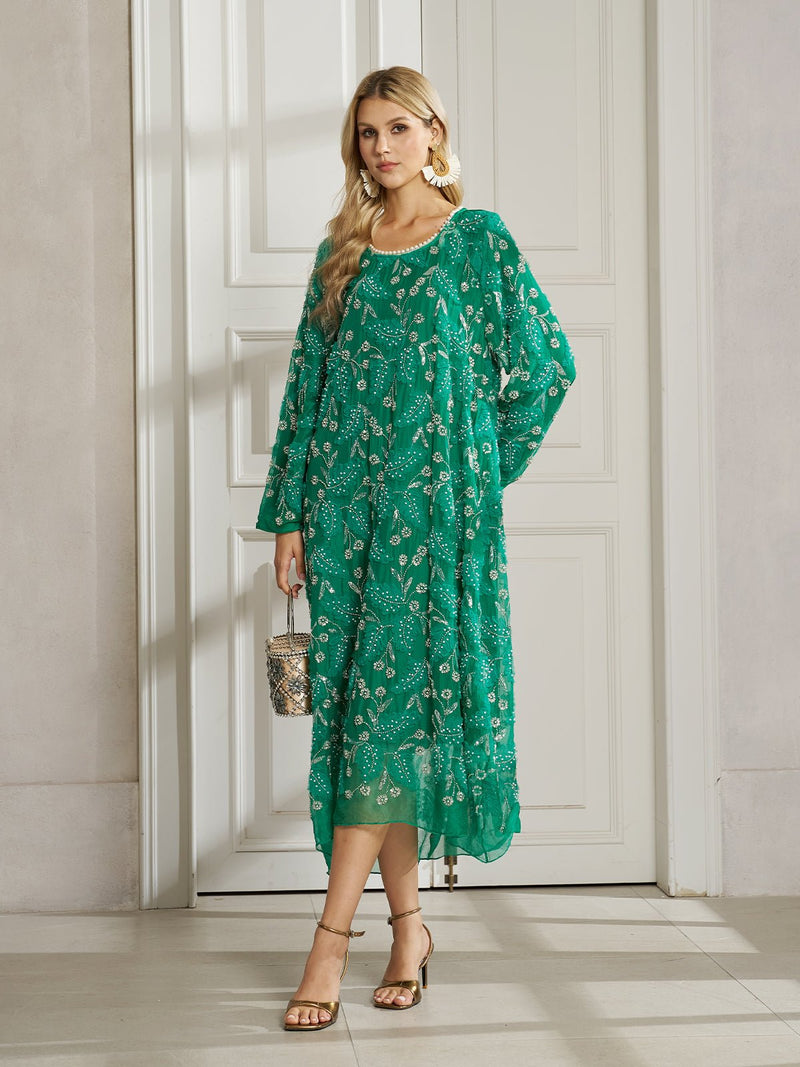 A woman stands indoors by white double doors in the Social Queen 100% Silk Beaded Embroidery Dress, styled with gold earrings, sandals, and a small handbag—a perfect wedding guest look.