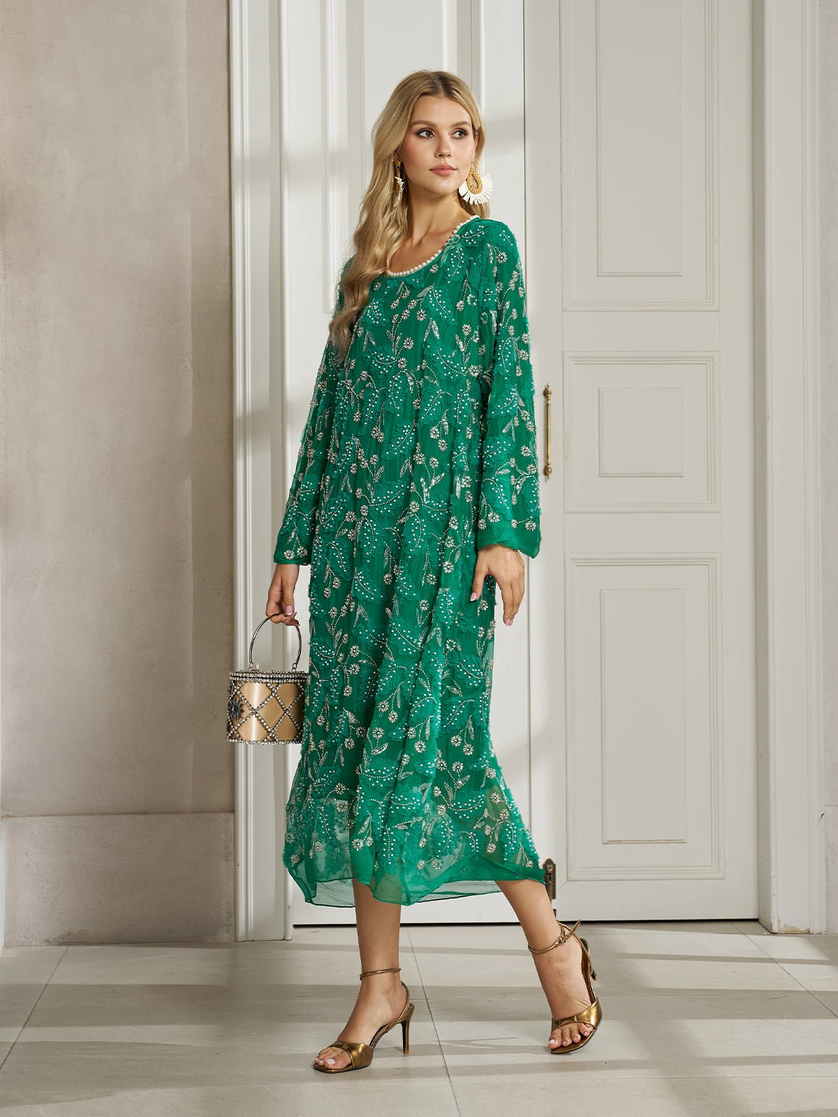 A woman stands indoors wearing the Social Queen 100% Silk Beaded Embroidery Dress with long sleeves. She holds a small handbag and complements her look with gold sandals.