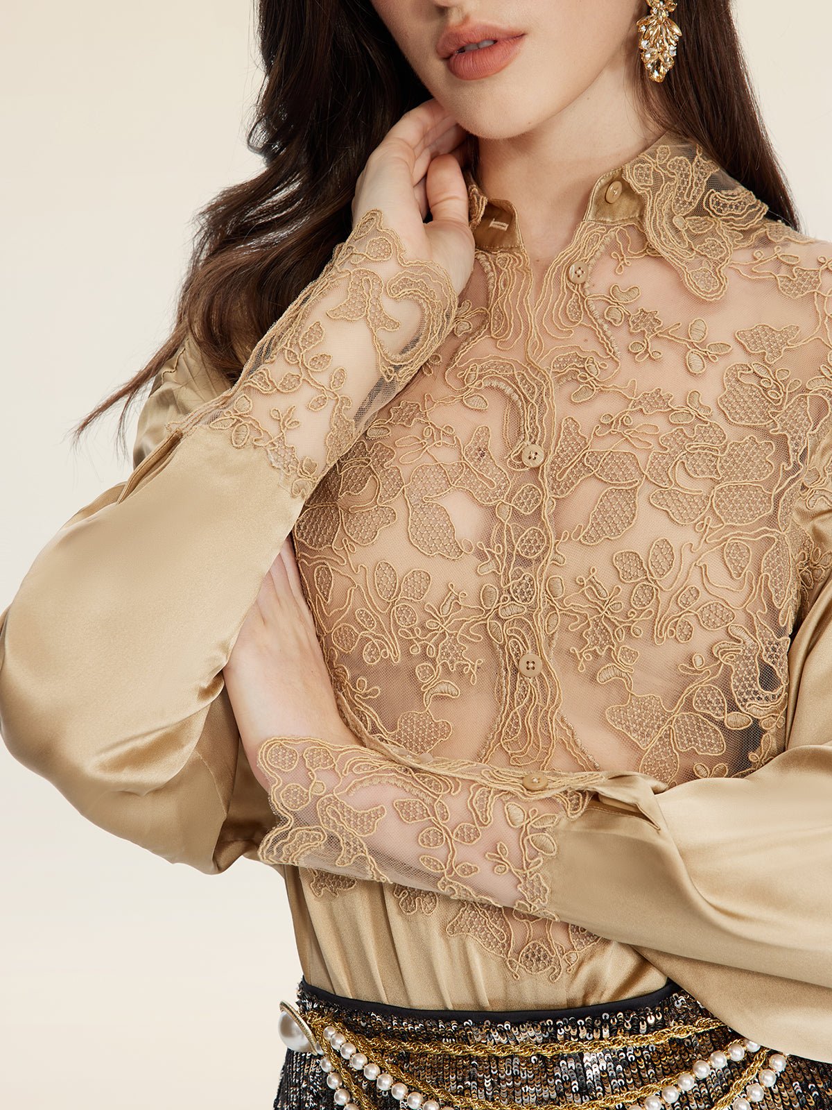 A woman in the Social Queen 100% Silk Embroidered Lace Satin Blouse crosses her arms, accessorizing with gold earrings and a pearl-decorated belt.