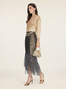 A woman in profile wears the Social Queen 100% Silk Embroidered Lace Satin Blouse, a black sequin fringe skirt, gold heels, statement earrings, and carries a small gold handbag with pearl details.