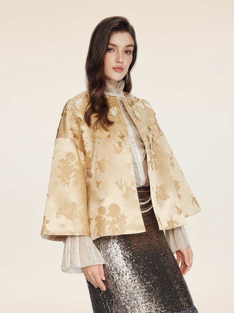 A woman models the Social Queen 100% Silk Floral Embroidered Satin Jacket over a sheer blouse and silver sequined skirt, posing against a plain light background.