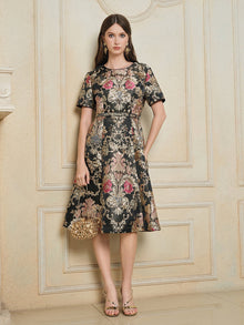A woman stands indoors against an ornate cream wall, wearing the Social Queen 100% Silk Jacquard Satin Gold Embroidered Floral Dress, paired with a gold handbag and gold sandals.