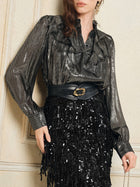 A person wearing Social Queen’s 100% Silk Luminous Metallic Ruffle Blouse, paired with a wide black belt featuring a gold buckle and a black sequined fringe skirt.