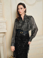 A woman wears Social Queen's 100% Silk Luminous Metallic Ruffle Blouse with puff sleeves, paired with a black belted sequin skirt and statement earrings, standing indoors against a cream-colored wall.