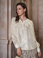 A woman in the Social Queen 100% Silk Luminous Metallic Ruffle Blouse pairs it with a gold sequin skirt, standing by an ornate wall and looking to the side.