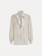 The Social Queen 100% Silk Metallic Ribbon-Tie Blouse features long puff sleeves, a cream hue, a button-down front, and a large bow at the neck, shown on a plain white background.