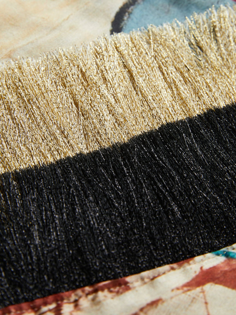 Close-up of the Social Queen 100% Silk Print Tassel Chain Belt, showcasing a thick fringe border and tassel accents with a cream upper section and black lower section, displayed on a patterned surface.