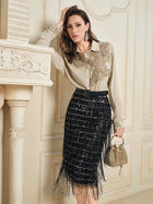 A woman poses indoors in a Social Queen 100% Silk Retro Floral Appliqué Satin Blouse, a black fringed skirt, earrings, and a gold handbag, leaning on a white mantelpiece and radiating French vintage charm.