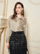 A woman wears the Social Queen 100% Silk Retro Floral Appliqué Satin Blouse with a black sequined skirt, standing indoors by a cream wall, radiating French vintage elegance.