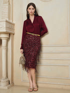 Indoors, a woman models Social Queen’s 100% Silk Satin Wrap V-Neck Blouse paired with a matching fringed skirt, gold sandals, and a small handbag beside an ornate cream fireplace, highlighting its versatile styling.