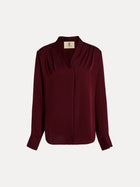 The Social Queen 100% Silk Satin Wrap V-Neck Blouse in burgundy features long sleeves, pleated shoulders, buttoned cuffs, and a cross-front design. Shown on a plain white background, it's ideal for versatile styling.