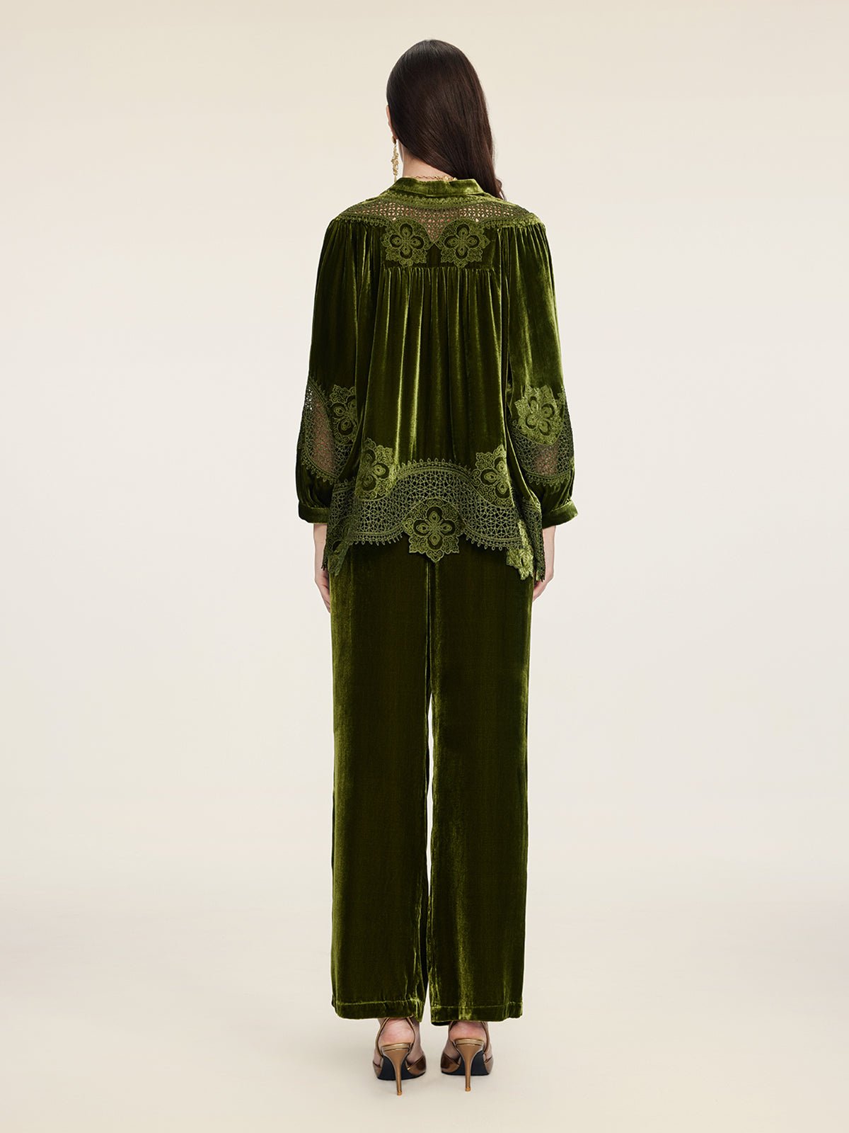 A person stands facing away, wearing the Social Queen 100% Silk Velvet Lace-Panel Blouse in green with hand-stitched lace, styled with matching wide-leg pants and heeled sandals.
