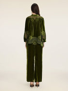 A person stands facing away, wearing the Social Queen 100% Silk Velvet Lace-Panel Blouse in green with hand-stitched lace, styled with matching wide-leg pants and heeled sandals.