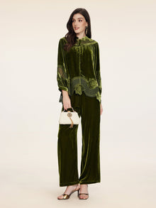 A woman wears the Social Queen 100% Silk Velvet Lace-Panel Blouse in green with matching wide-leg pants, accessorized with a white handbag and metallic heels, standing against a plain background.