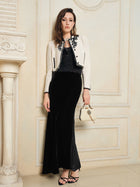 A woman stands indoors in a black 100% Silk Velvet & Tulle Mermaid Skirt by Social Queen, styled with a cream embroidered jacket, a small handbag, and strappy sandals for vintage-inspired elegance.