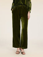 A person stands against a plain background wearing Social Queen’s 100% Silk Velvet Wide-Leg Pants in olive green with brown strappy heels, hands casually in their pockets.