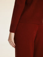 A person wears Social Queen's 100% Wool Knit Elastic Trousers in dark red, styled with a matching ribbed long-sleeve top. They're shown from shoulder to knee, one arm at their side, highlighting the trousers' straight-leg silhouette.