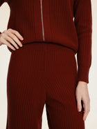 A person wears Social Queen's 100% Wool Knit Elastic Trousers in maroon, featuring a straight-leg silhouette and elastic waist, paired with a matching ribbed sweater. One hand rests on their waist, the other by their side.