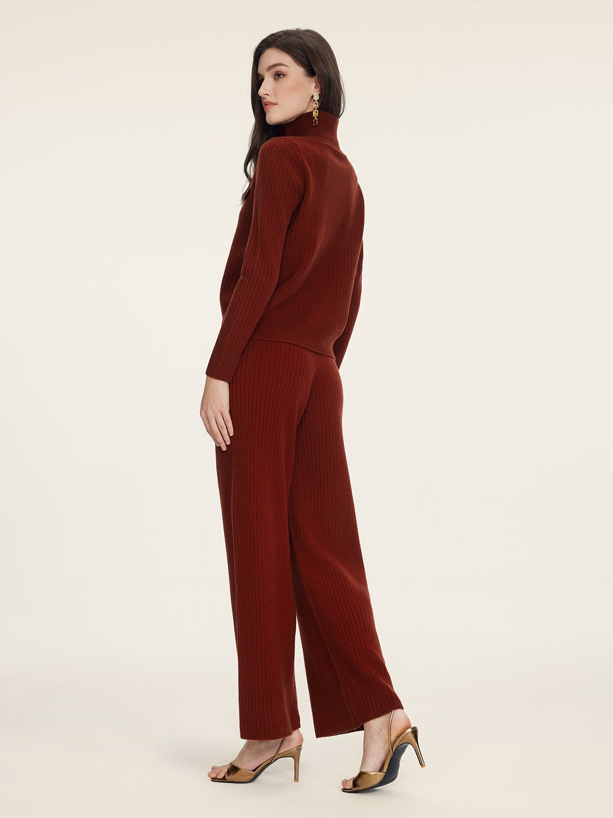 A woman in profile wears Social Queen’s 100% Wool Knit Elastic Trousers in rust, paired with a matching turtleneck sweater and heeled sandals, set against a plain background.