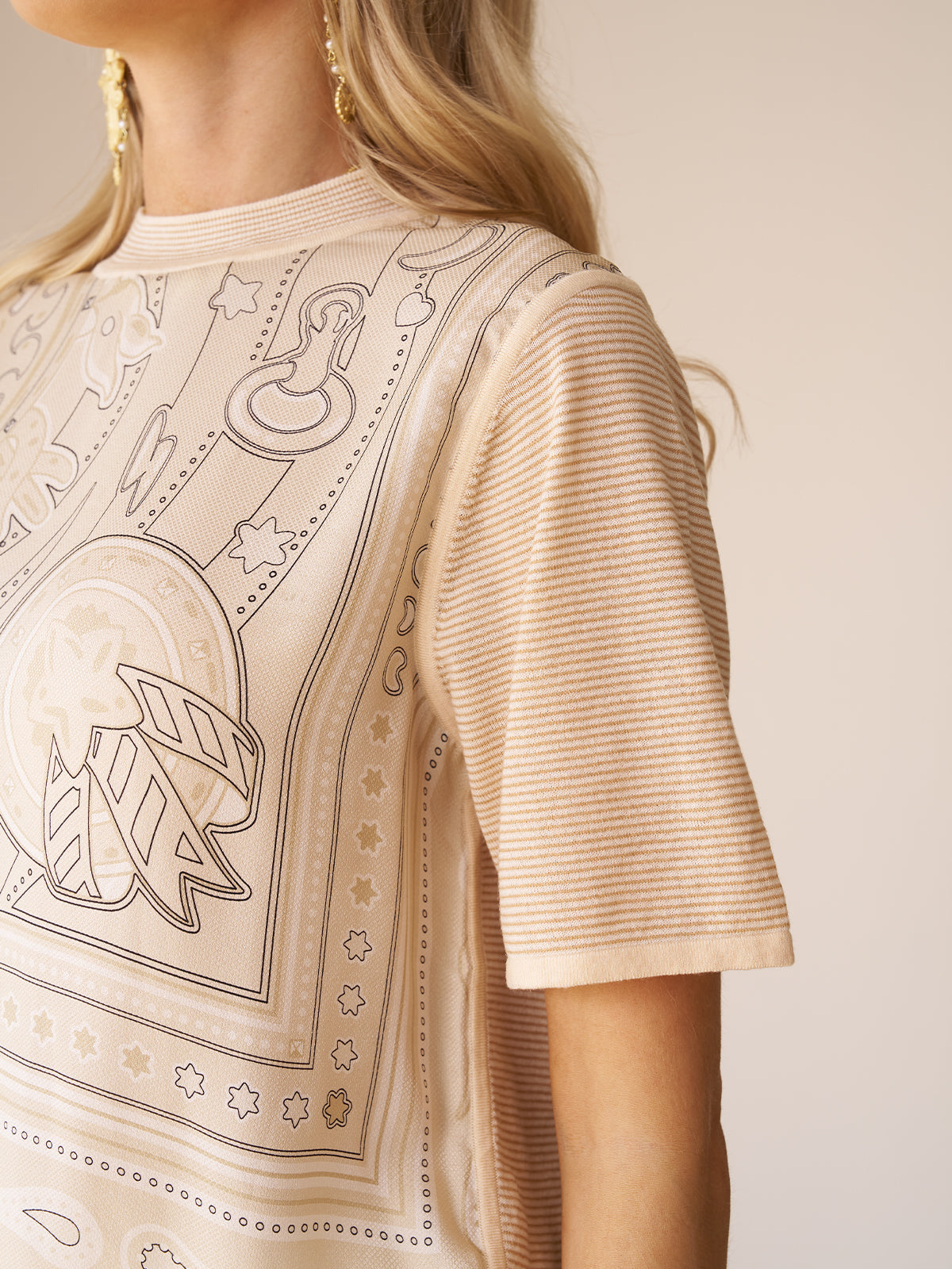 A close-up of a woman wearing the Social Queen Paisley Print Patchwork Top, a lightweight knit beige t-shirt featuring a paisley print and striped short sleeves.