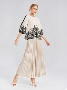 A woman poses against a plain light background wearing a cream top with black botanical prints, Social Queen Striped Pleated Wide-Leg Pants in beige, and white heeled sandals.