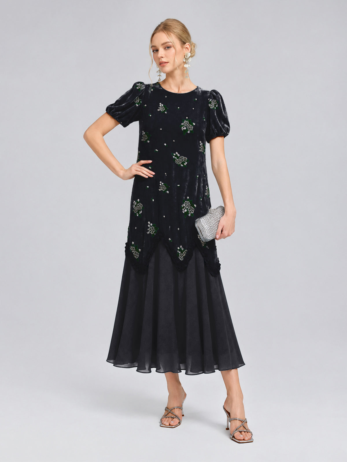A woman stands against a plain background, wearing the Social Queen Beaded Floral Silk Velvet Dress in navy blue velvet and chiffon with intricate beaded floral embroidery. She completes the look with a silver clutch and heels.