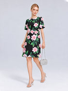 A woman stands against a plain light gray background wearing the Social Queen 3D Peony Floral Shift Dress paired with clear heeled sandals and carrying a small silver handbag.