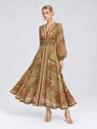 A woman stands against a plain background in heeled sandals, wearing the Social Queen Paisley Print Mulberry Silk Dress—an elegant olive-green floral piece featuring a V-neckline, long sleeves, and a flared skirt that’s perfect for resort wear.