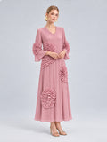 A woman wearing the Social Queen 3D Floral Pleated Dress—an elegant, long pink maxi dress featuring pleats and large, textured floral appliqué embellishments—stands against a plain light background.