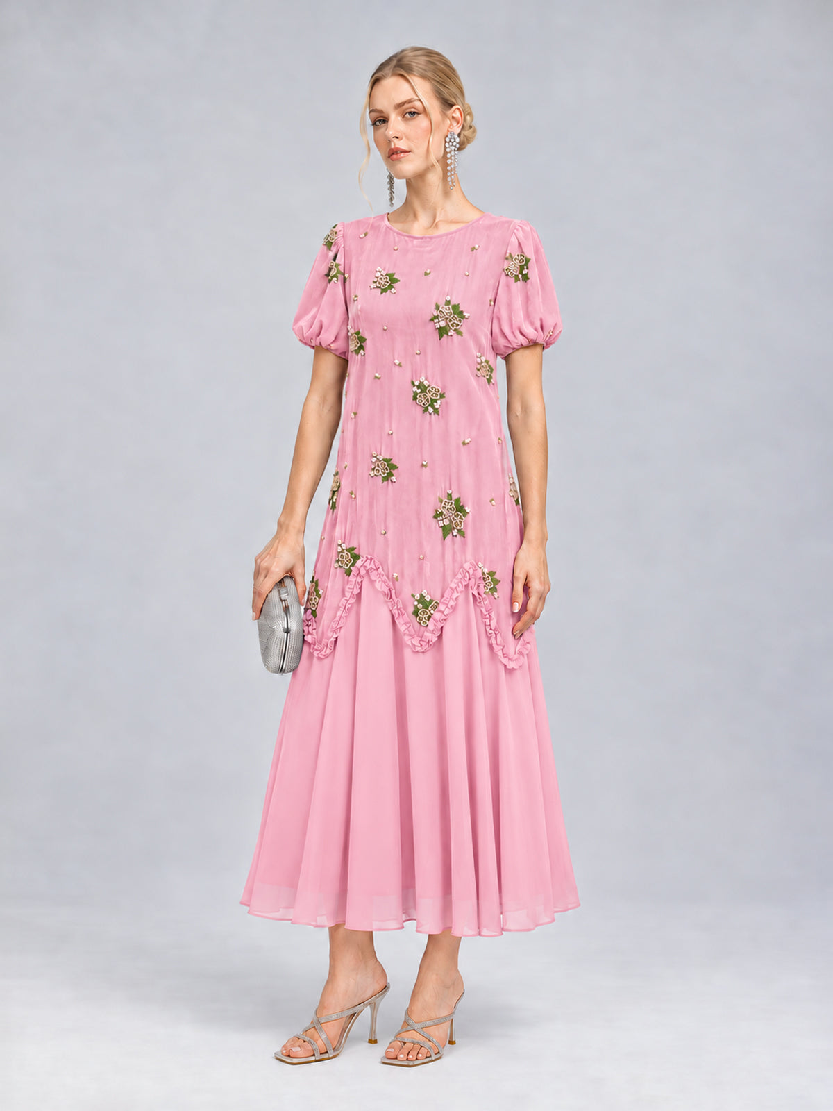 A woman stands against a plain gray background wearing the Social Queen Beaded Floral Silk Velvet Dress—a pink, silk-blend velvet dress featuring beaded floral embroidery and short sleeves—paired with silver heels and a small silver clutch.