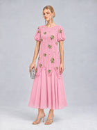 A woman stands against a plain gray background wearing the Social Queen Beaded Floral Silk Velvet Dress—a pink, silk-blend velvet dress featuring beaded floral embroidery and short sleeves—paired with silver heels and a small silver clutch.