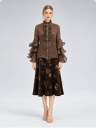 A woman stands facing forward, wearing the Pleated Layered Ruffle Blouse from Social Queen—a brown blouse with layered ruffle sleeves crafted from lightweight polyester chiffon—paired with a dark floral midi skirt and strappy beige heels against a neutral background.