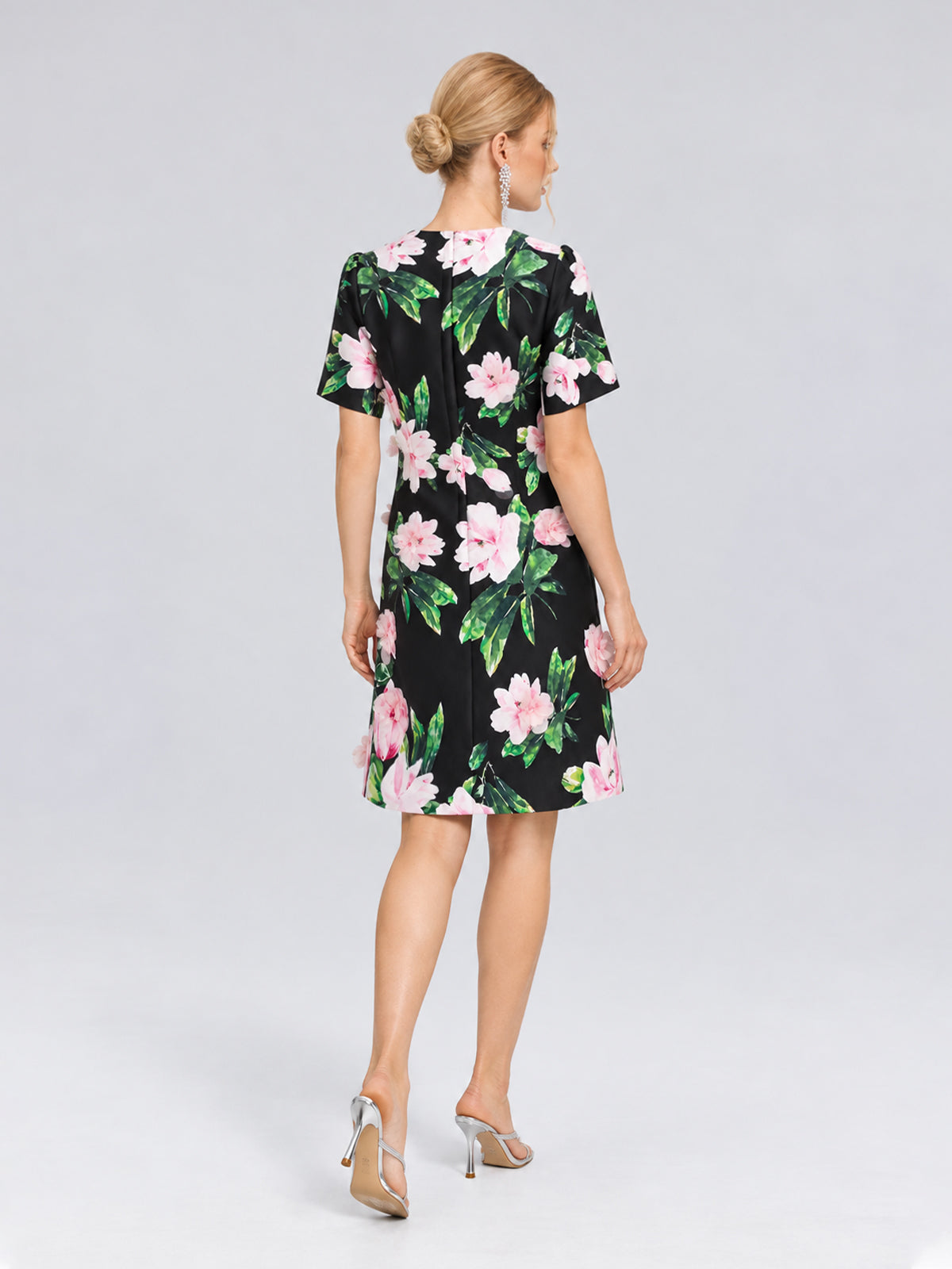 A woman with blonde hair in a bun is seen from behind wearing the Social Queen 3D Peony Floral Shift Dress, featuring a black base with pink peony prints, paired with silver high heels.