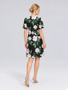A woman with blonde hair in a bun is seen from behind wearing the Social Queen 3D Peony Floral Shift Dress, featuring a black base with pink peony prints, paired with silver high heels.